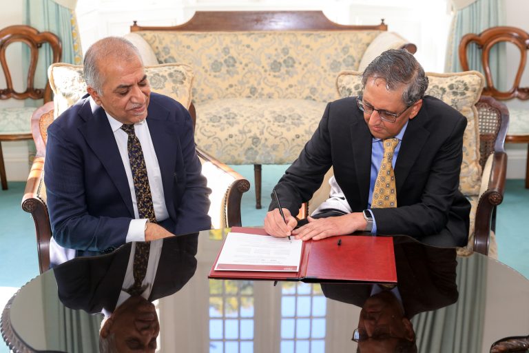 Abhey and Mehta sitting at a table signing a document